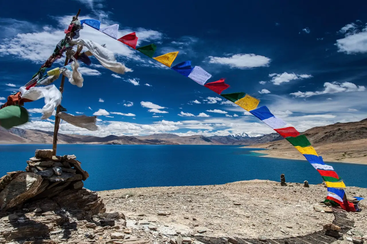 Voyage en Asie — Lac turquoise au Ladakh à Korzok Phu, entouré de montagnes désertiques et de drapeaux de prière bouddhistes tibétains.