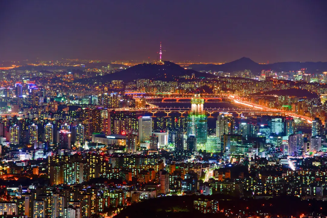 Un panorama nocturne de la ville de Séoul illuminée avec la tour N Seoul Tower éclairée sur sa colline en arrière-plan.