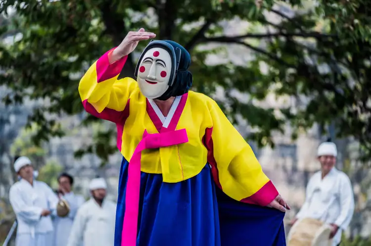 Un artiste en hanbok coloré effectuant la danse traditionnelle des masques d'Hahoe devant des musiciens à Andong.