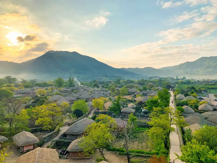 Une vue panoramique sur les toits de chaume du village traditionnel fortifié de Nagan Eupseong entouré de collines verdoyantes au coucher du soleil.