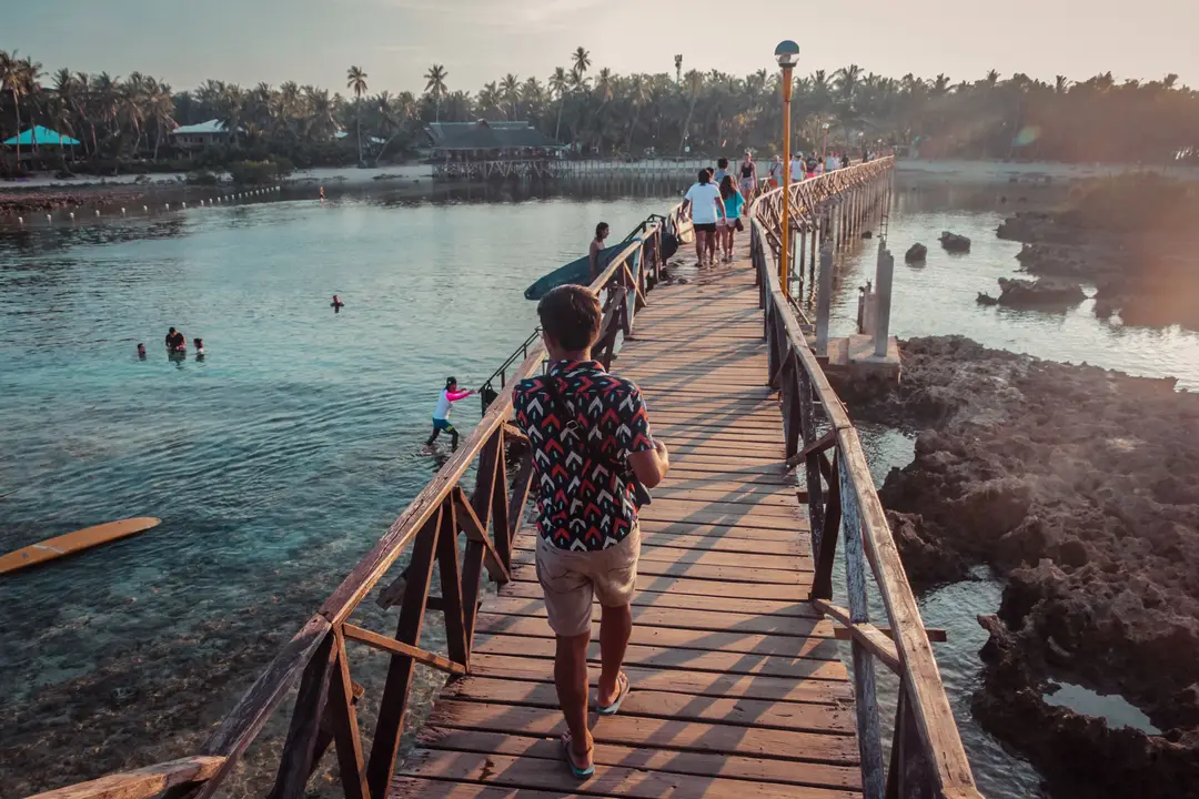 Des gens traversent un pont en bois pittoresque à General Luna, Philippines, au coucher du soleil.jpg