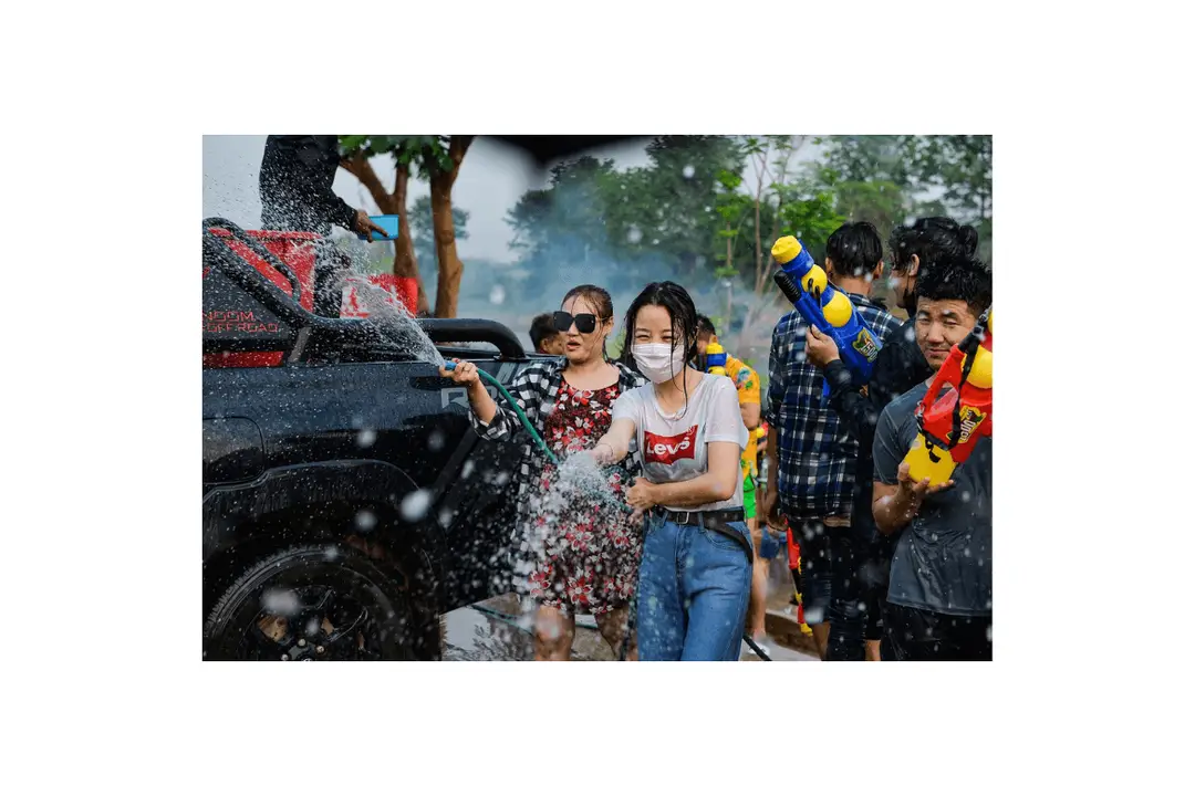 De joyeux jets d'eau projetés en l'air et retombant en gouttes étincelantes sur la foule réunie sur le parvis d'un temple bouddhiste thaïlandais doré à Chiang Mai sous un grand ciel bleu.