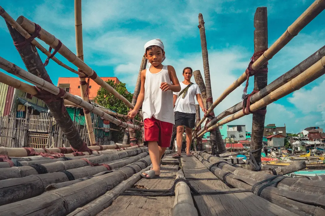 Deux enfants traversent un pont de bambou rustique à Navotas, Manille, Philippines, par une journée ensoleillée