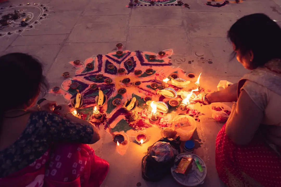 Deux femmes créent un rangoli coloré et allument des diyas pour la célébration de Diwali, mettant en avant la culture et la tradition indiennes.jpg