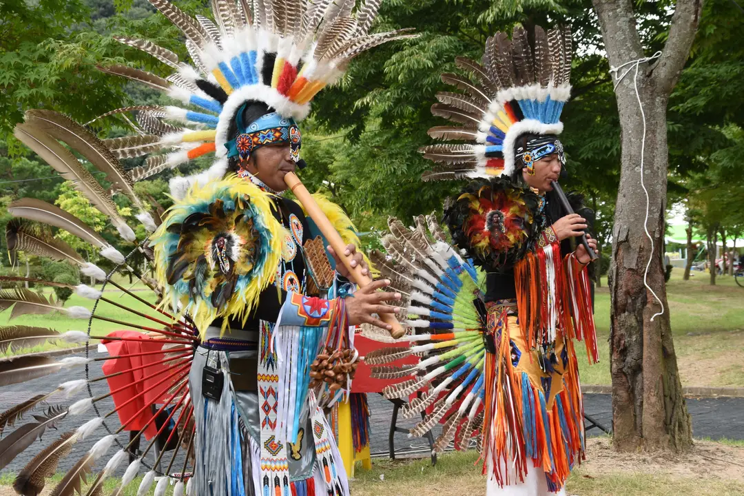 Deux participants en tenue traditionnelle avec des instruments de musique lors d’un rassemblement culturel autochtone.