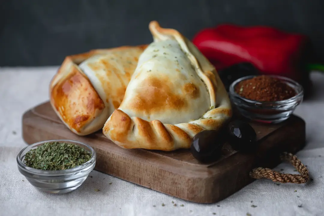 Empanadas dorées sur une planche en bois avec des herbes et des épices