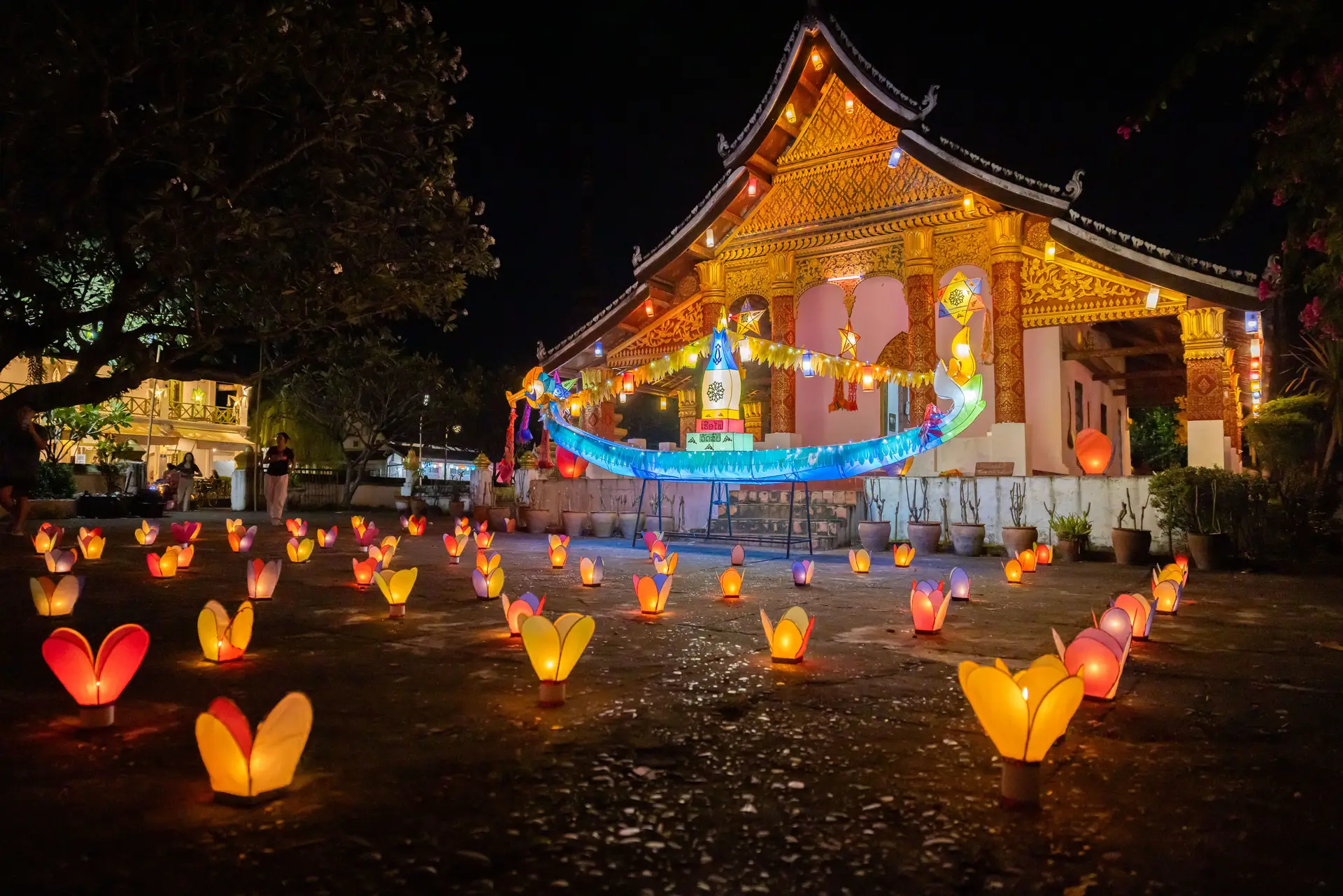 Temple laotien illuminé de lanterne et bougies au sol lors de la fête des lumières Lai Heua Fai à Luang Prabang.