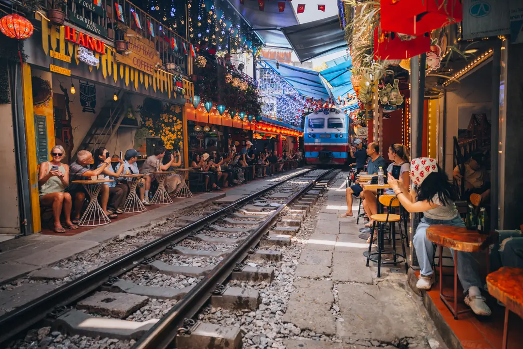 Des touristes assis aux tables des cafés alignés le long des rails étroits de la célèbre rue du train à Hanoi, sous des lanternes et des drapeaux vietnamiens rouges.