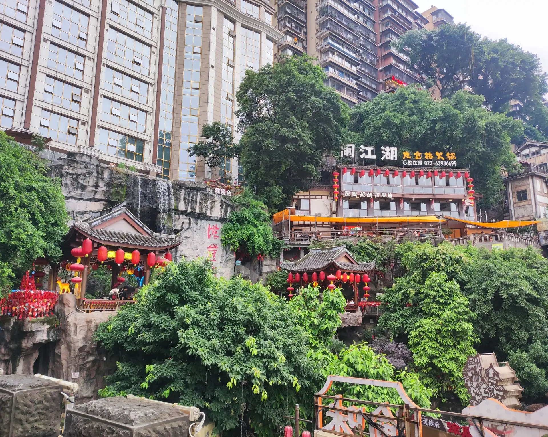 batiments traditionnels aux lanternes rouges construits sur une falaise verdoyante au pied de grands immeubles modernes a chongqing