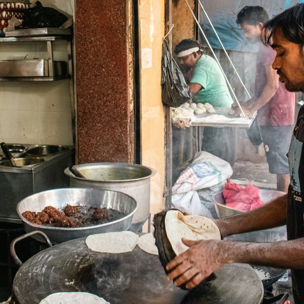 Un cuisinier de rue à Mumbai prépare des pains plats traditionnels sur une plaque chauffante circulaire dans une cuisine ouverte animée.