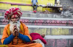 Voyager en Inde – Sadhu en tenue traditionnelle orange les mains jointes en prière sur les ghats de Varanasi.