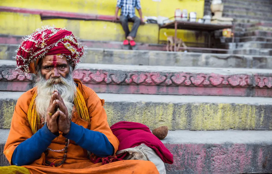 Voyager en Inde – Sadhu en tenue traditionnelle orange les mains jointes en prière sur les ghats de Varanasi.