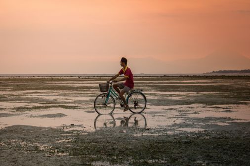 Voyage en Asie — Cycliste à Bali sur une étendue d'eau peu profonde au coucher du soleil avec reflet parfait.