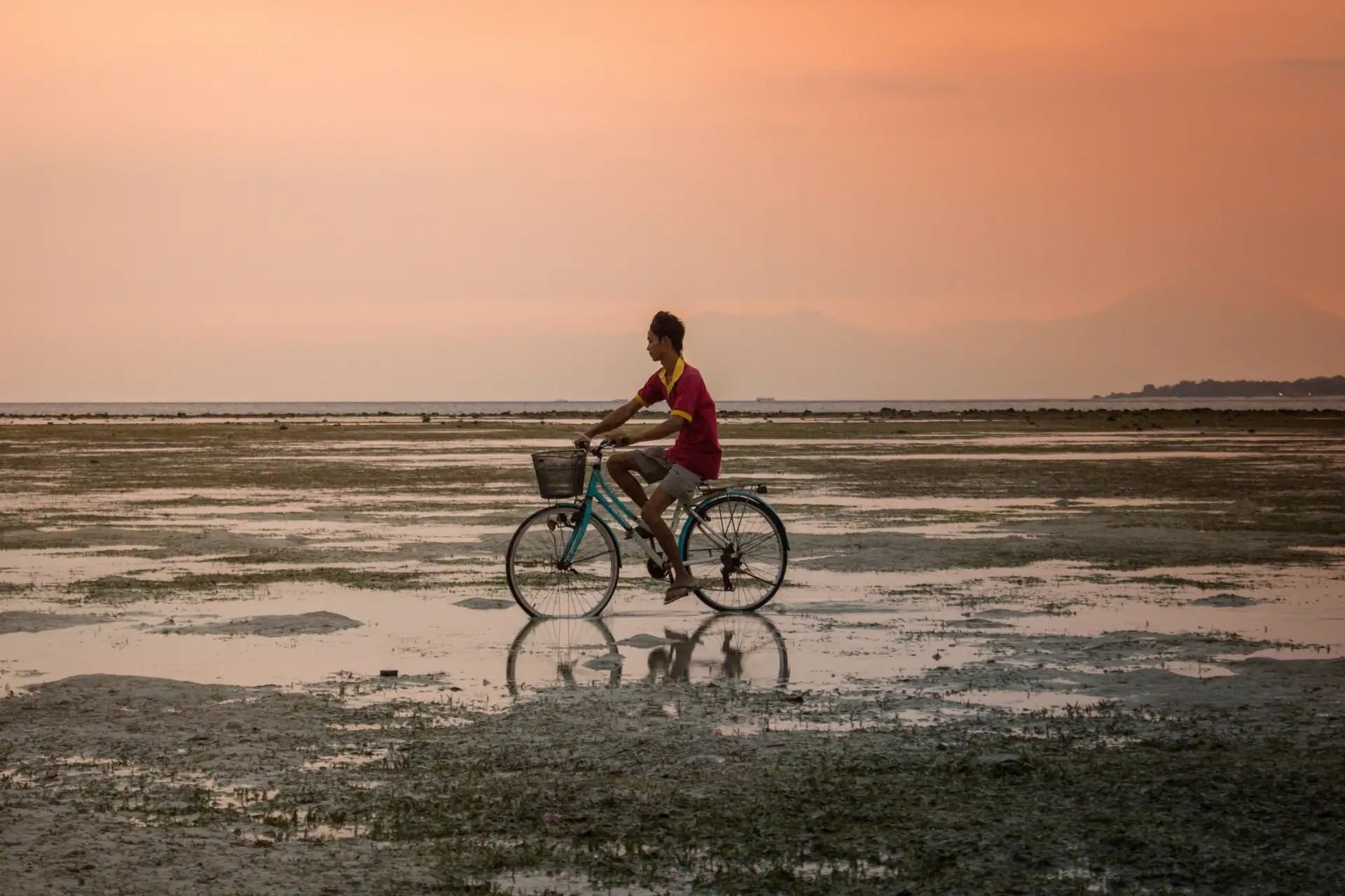 Voyage en Asie — Cycliste à Bali sur une étendue d'eau peu profonde au coucher du soleil avec reflet parfait.