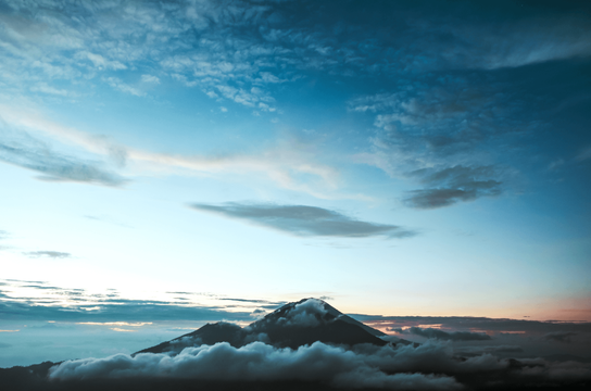 Voyage en Asie — Cycliste balinais en sarong et caping sur un vélo dans un village avec maisons en bambou et chaume.