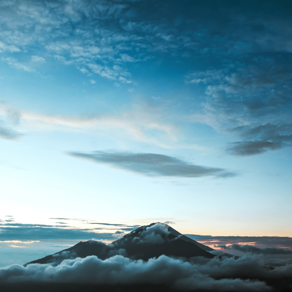 Voyage en Asie — Cycliste balinais en sarong et caping sur un vélo dans un village avec maisons en bambou et chaume.
