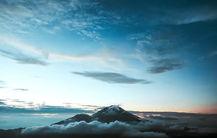 Voyage en Asie — Cycliste balinais en sarong et caping sur un vélo dans un village avec maisons en bambou et chaume.