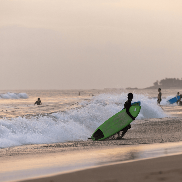 Voyage en Asie — Surfeurs à Bali au coucher du soleil sur une plage avec vagues et sable foncé.