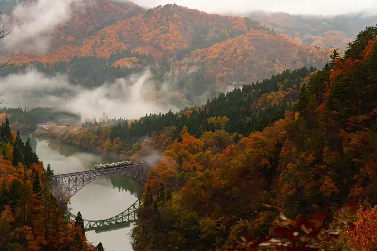 pont de chemin de fer panoramique traversant une riviere au milieu de collines forestieres en automne avec brume au japon