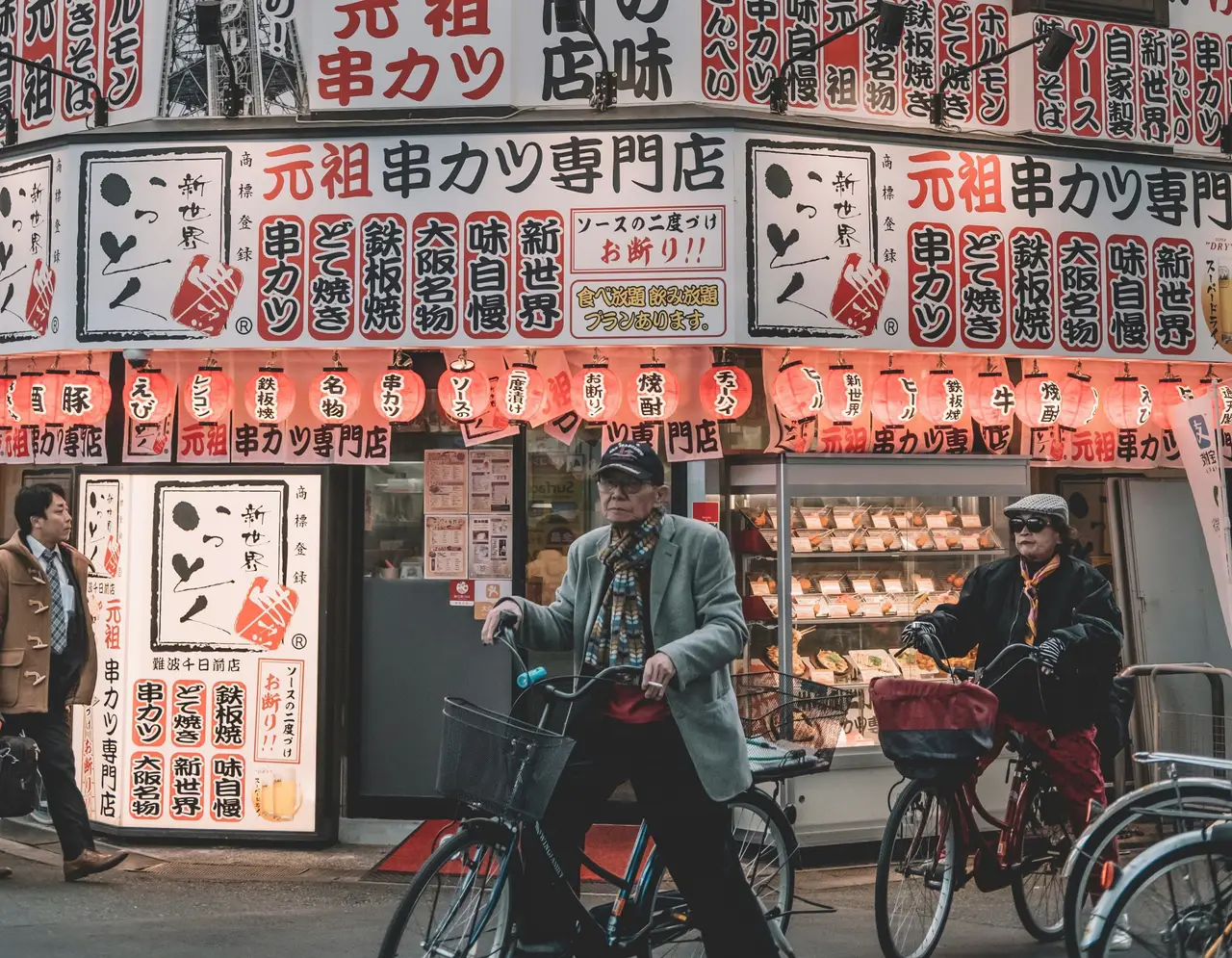 Ein Paar fährt mit dem Fahrrad durch eine traditionelle Straße mit japanischen Werbeschildern in Kyoto