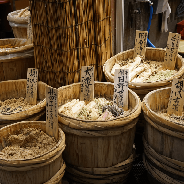 Étal de légumes en saumure traditionnels (Tsukemono) présentés dans des seaux en bois au marché de Nishiki à Kyoto, une immersion gastronomique authentique conseillée par les experts Shanti Travel.