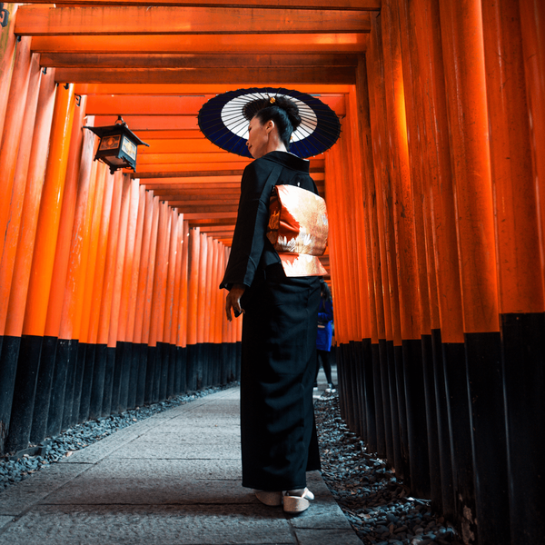 Femme vêtue d'un kimono traditionnel marchant sous les milliers de portails torii vermillon du sanctuaire Fushimi Inari-taisha à Kyoto, une immersion culturelle profonde incluse dans les circuits Shanti Travel.
