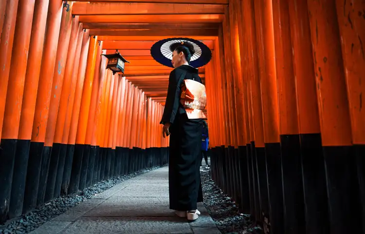 Femme vêtue d'un kimono traditionnel marchant sous les milliers de portails torii vermillon du sanctuaire Fushimi Inari-taisha à Kyoto, une immersion culturelle profonde incluse dans les circuits Shanti Travel.