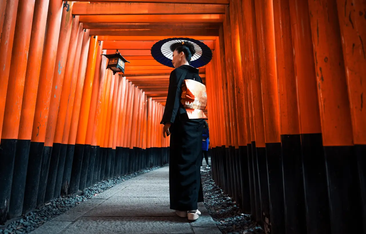Femme vêtue d'un kimono traditionnel marchant sous les milliers de portails torii vermillon du sanctuaire Fushimi Inari-taisha à Kyoto, une immersion culturelle profonde incluse dans les circuits Shanti Travel.