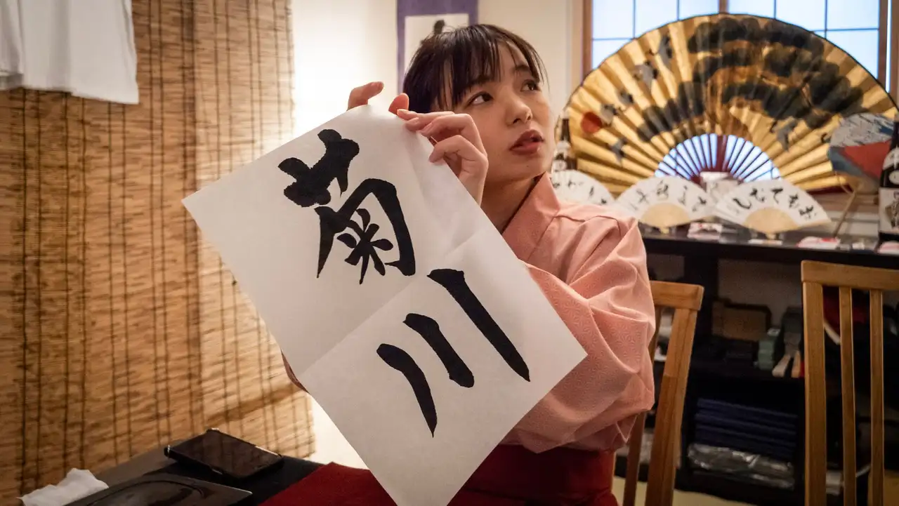 Une jeune femme en tenue traditionnelle présentant une œuvre de calligraphie japonaise réalisée à l'encre lors d'un atelier culturel.
