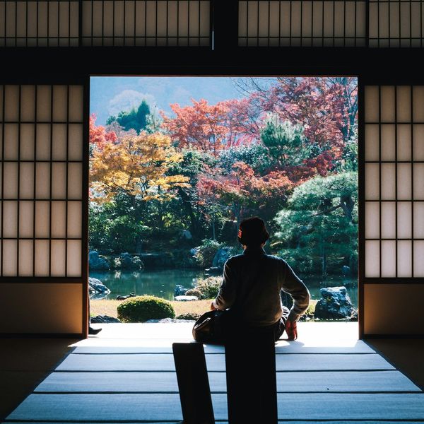Travel in Asia - A man seated in temple building with open shoji screen doors looking out over autumn colors in Japan
