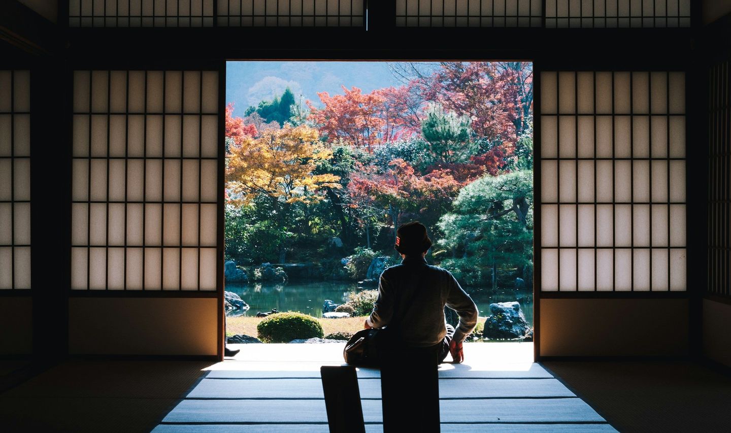Travel in Asia - A man seated in temple building with open shoji screen doors looking out over autumn colors in Japan