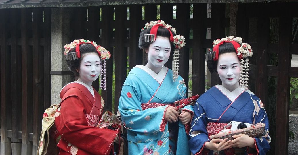 Trois Geishas et Maikos en kimono traditionnel devant une maison en bois à Kyoto, Japon.