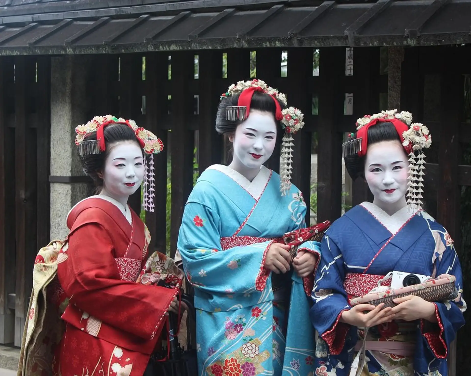 Trois Geishas et Maikos en kimono traditionnel devant une maison en bois à Kyoto, Japon.