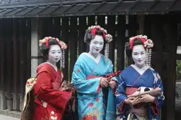 Trois Geishas et Maikos en kimono traditionnel devant une maison en bois à Kyoto, Japon.