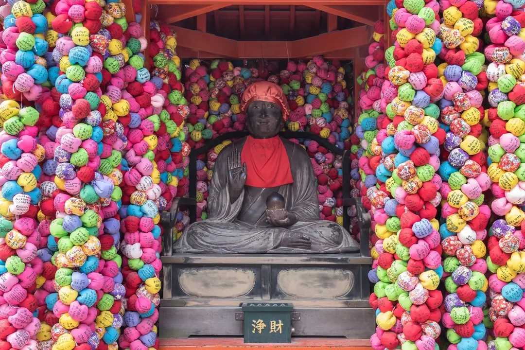 Statue bouddhiste entourée de centaines de boules de tissu colorées kukurizaru au sanctuaire Yasaka Koshin-do à Kyoto