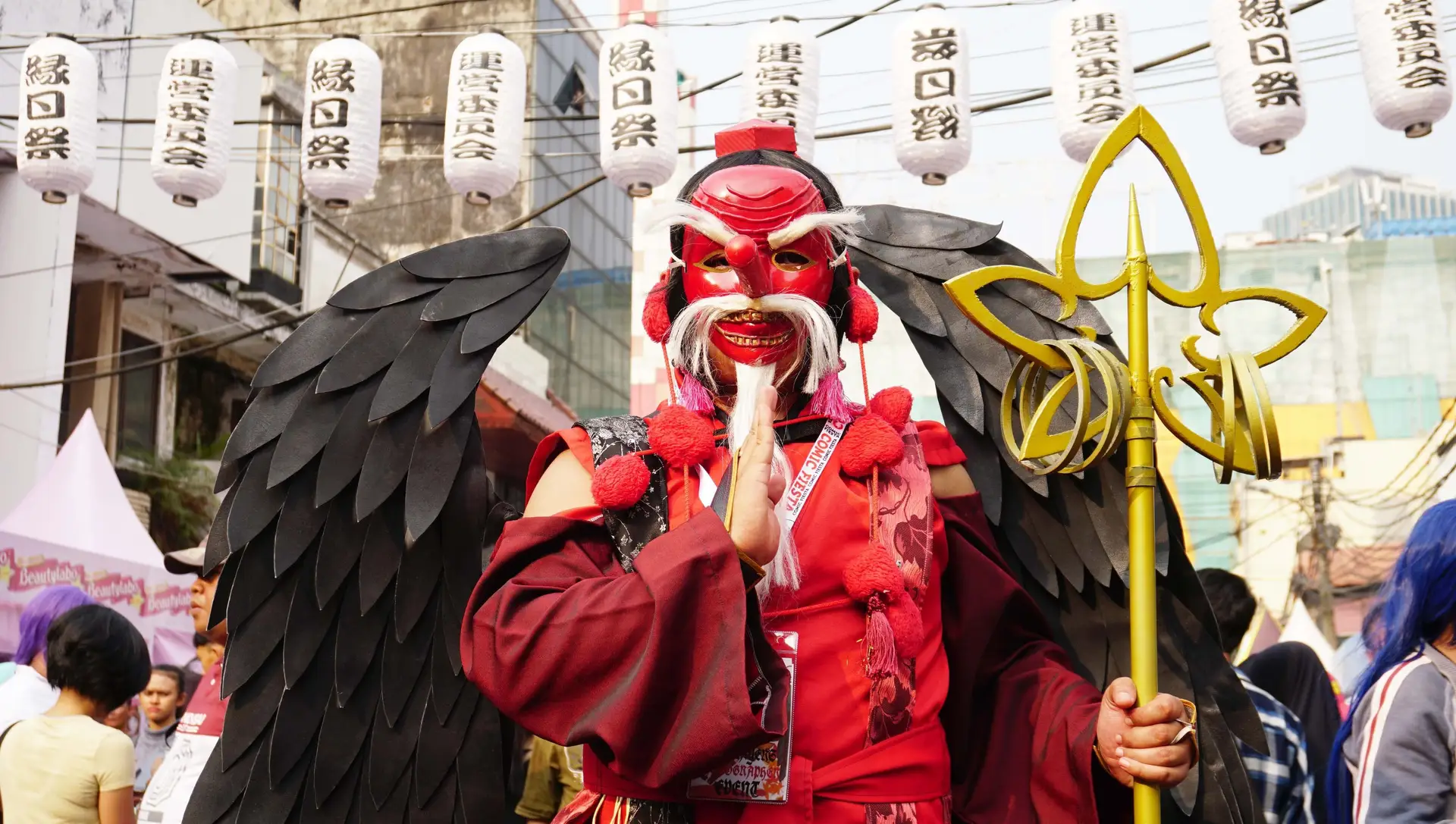 Voyage au Japon – Un participant costumé en Tengu avec un masque rouge au long nez, des ailes noires et un sceptre doré lors d'un festival de matsuri d'été.
