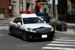Voiture de police japonaise patrouillant dans une rue urbaine, symbole de la sécurité et de la police de proximité au Japon.