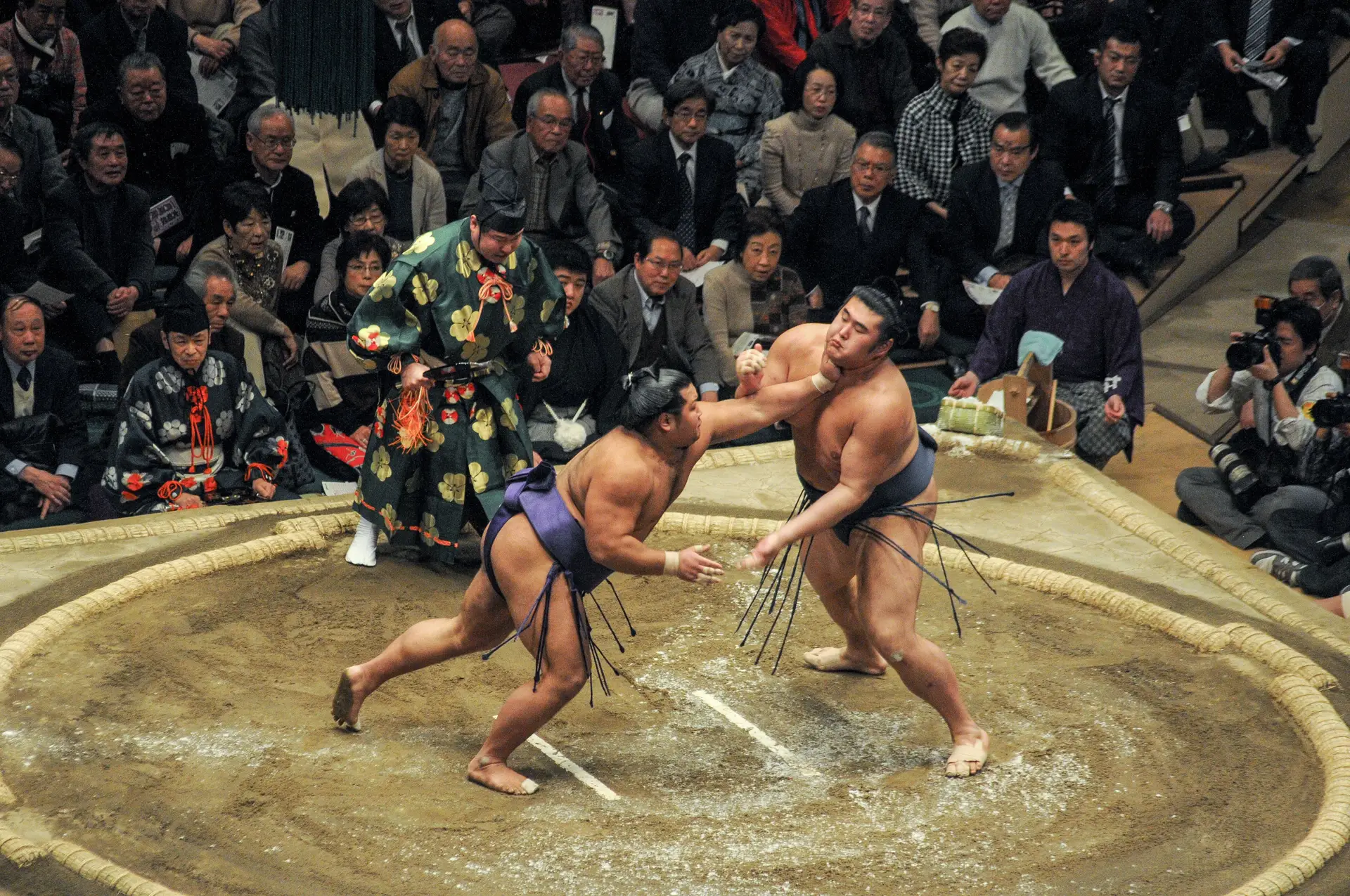 Voyage en Asie – Deux lutteurs de sumo s'affrontent sur le dohyo lors d'un tournoi traditionnel au Japon sous les yeux du public.