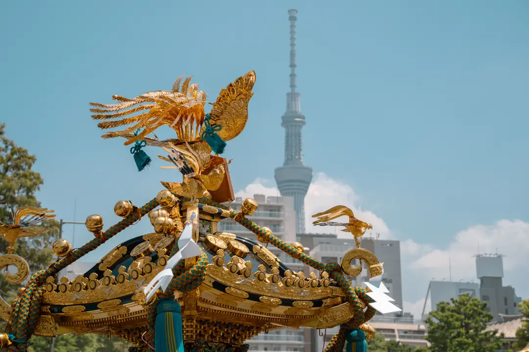 Voyage au Japon – Les sculptures dorées et détaillées du toit d'un mikoshi traditionnel lors d'un matsuri avec la tour Tokyo Skytree en arrière-plan.