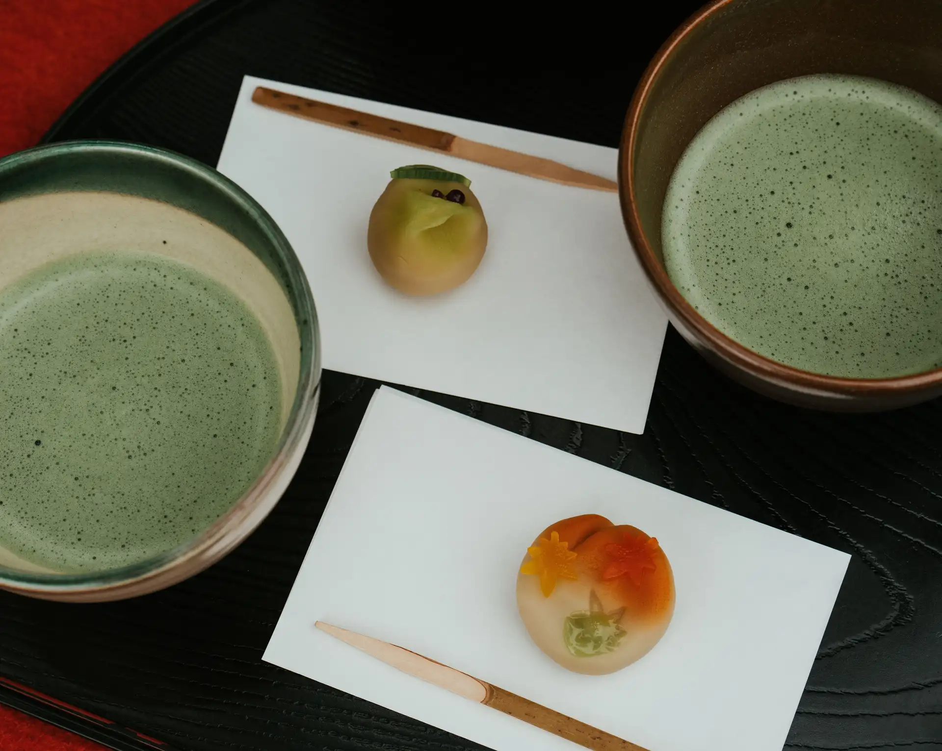 Route du thé au Japon – Deux bols de thé matcha moussant accompagnés de pâtisseries traditionnelles wagashi sur un plateau.