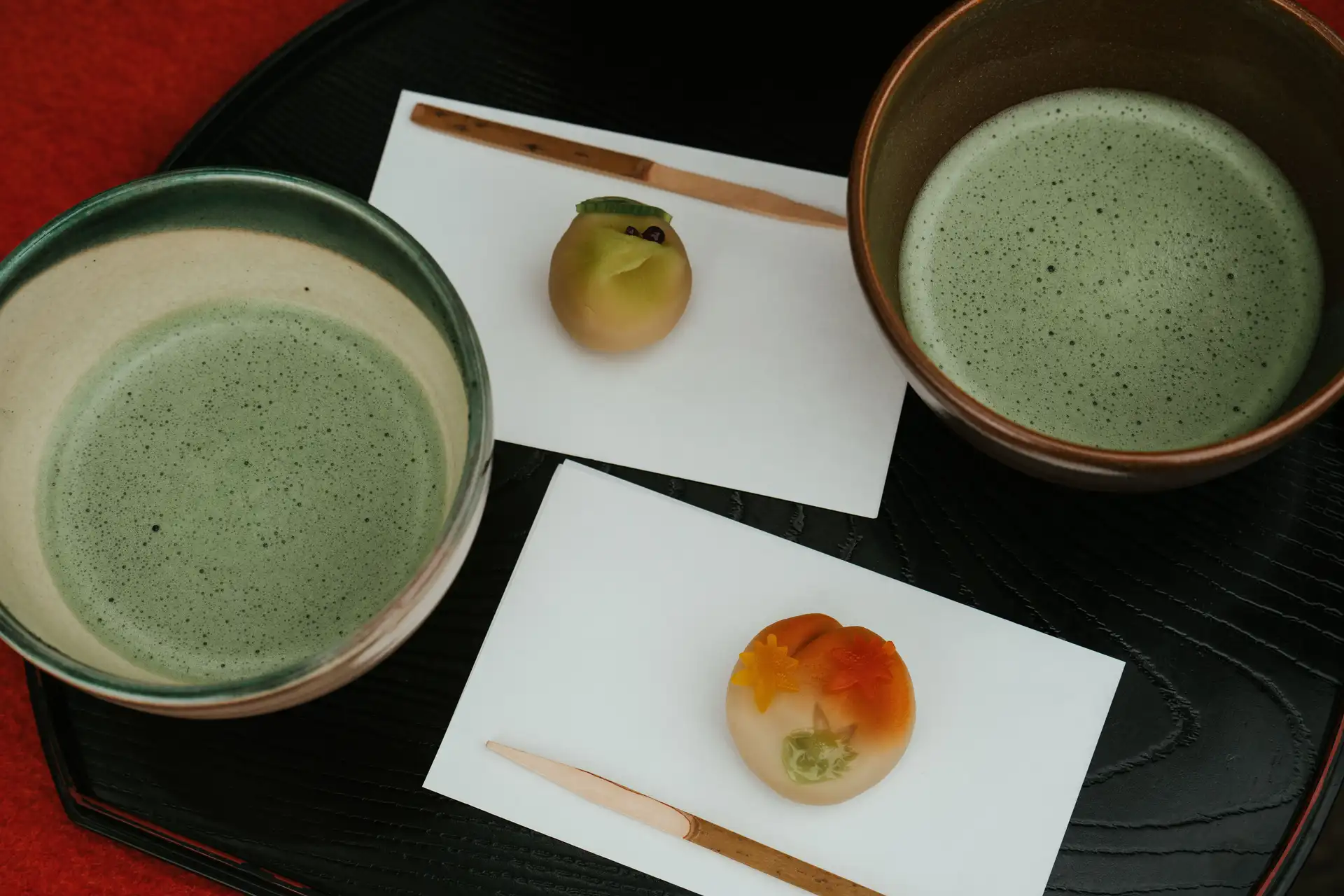 Route du thé au Japon – Deux bols de thé matcha moussant accompagnés de pâtisseries traditionnelles wagashi sur un plateau.