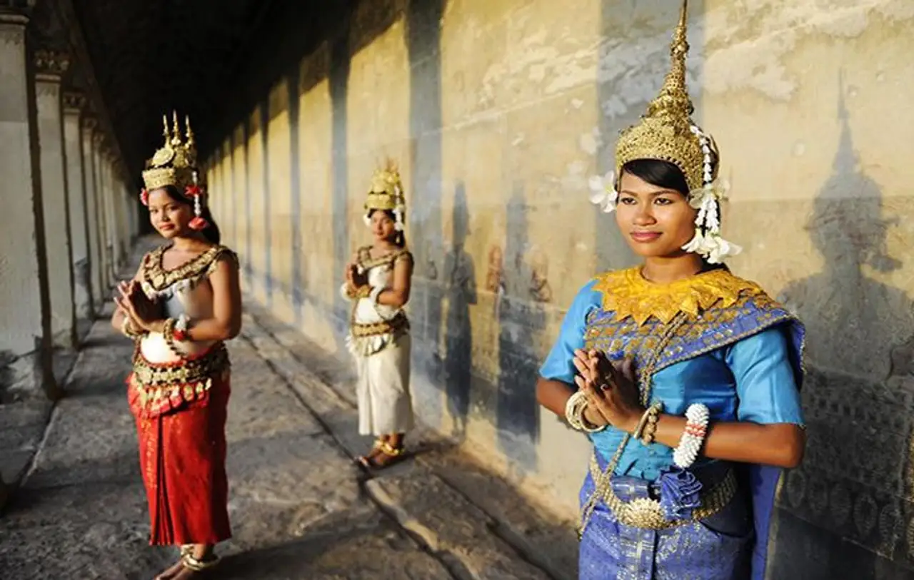 Trois danseuses traditionnelles khmères en costume de danse Apsara bleu et doré avec coiffes traditionnelles pointues, posant le long d'une galerie à colonnades en pierre au Cambodge.