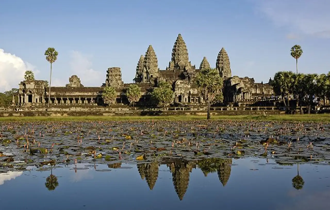 Les cinq tours en pierre en forme de lotus du temple d'Angkor Wat se reflétant parfaitement à la surface d'un bassin d'eau calme sous un ciel bleu au Cambodge.