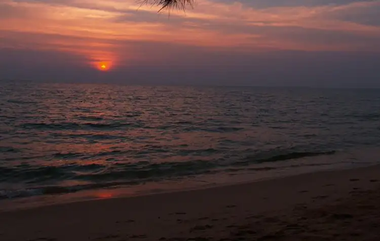 Un coucher de soleil rouge et orange se reflétant sur la surface de la mer qui borde une plage de sable fin à l'île de Koh Rong Sanloem au Cambodge.