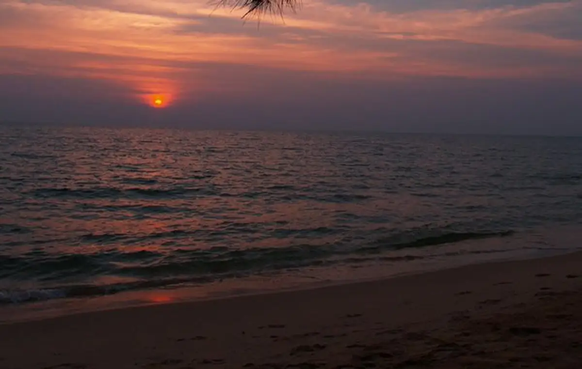 Un coucher de soleil rouge et orange se reflétant sur la surface de la mer qui borde une plage de sable fin à l'île de Koh Rong Sanloem au Cambodge.