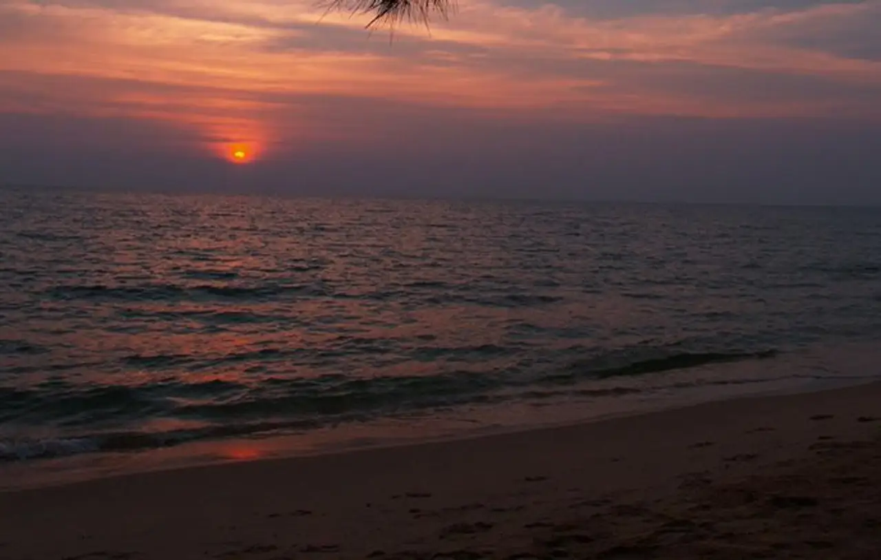 Un coucher de soleil rouge et orange se reflétant sur la surface de la mer qui borde une plage de sable fin à l'île de Koh Rong Sanloem au Cambodge.