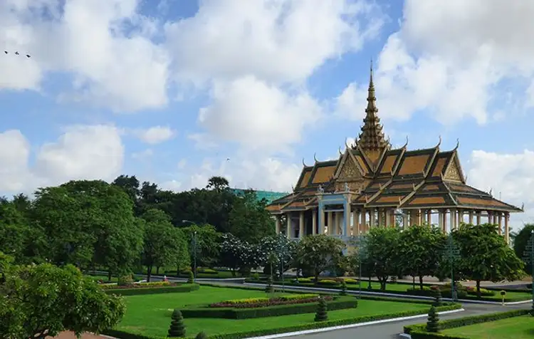 Le magnifique palais royal khmer aux toits dorés et à flèche pointue s'élevant au-dessus d'une ligne d'arbres et de jardins sous un ciel bleu nuageux à Phnom Penh.