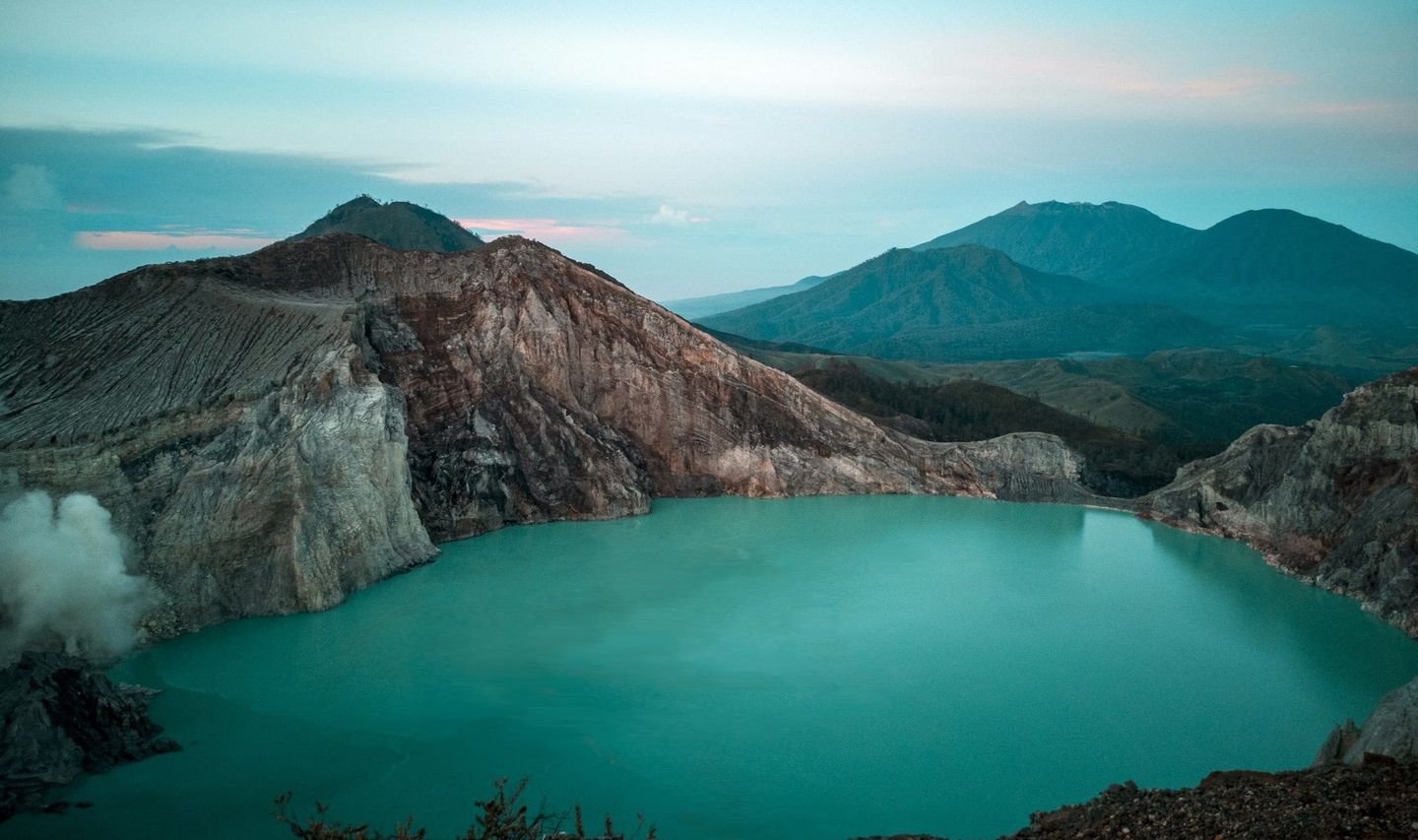 Voyage en Asie — Cratère du volcan Kawah Ijen à Java, Indonésie : lac turquoise laiteux et parois abruptes dans une ambiance dramatique.