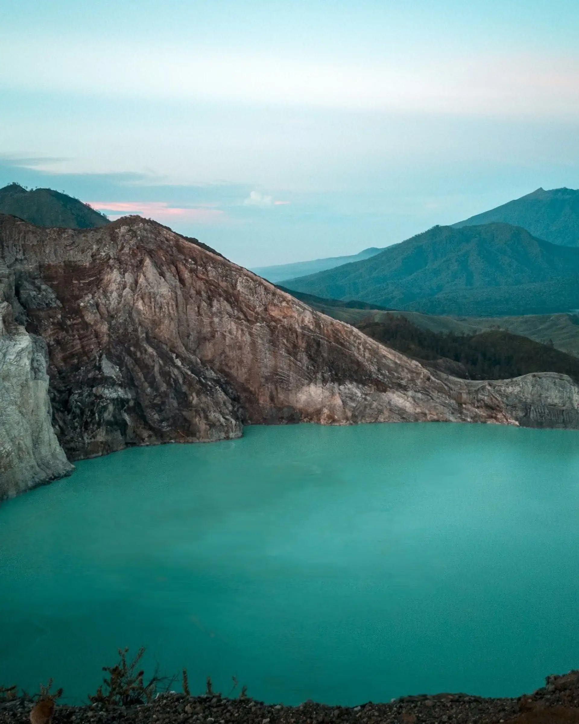 Voyage en Asie — Cratère du volcan Kawah Ijen à Java, Indonésie : lac turquoise laiteux et parois abruptes dans une ambiance dramatique.