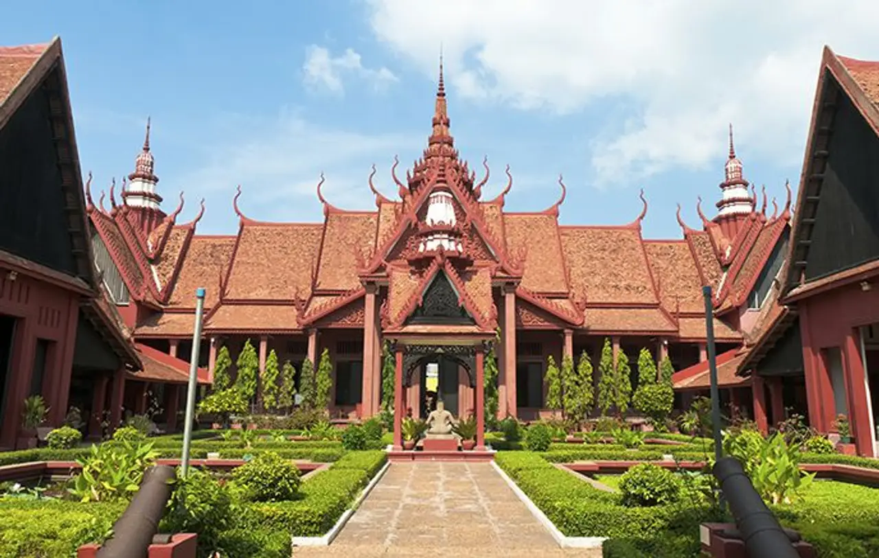 Façade architecturale en pierre rouge et toitures traditionnelles khmer sculptées du Musée National du Cambodge à Phnom Penh sous un ciel bleu parsemé de nuages.